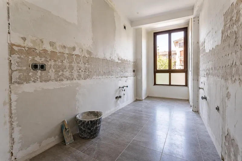 Visualización conceptual IA: Cocina sin muebles con paredes en preparación y zonas de enlucido.